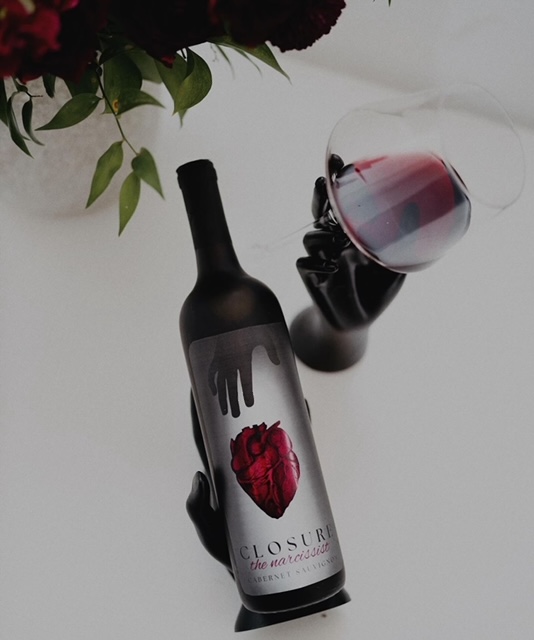 A wine bottle with an artistically designed label sits next to a glass of red wine.