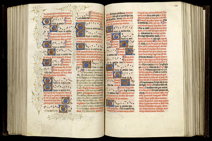 An open liturgical book with text in Latin and musical notations. The pages have decoration including borders and initials.