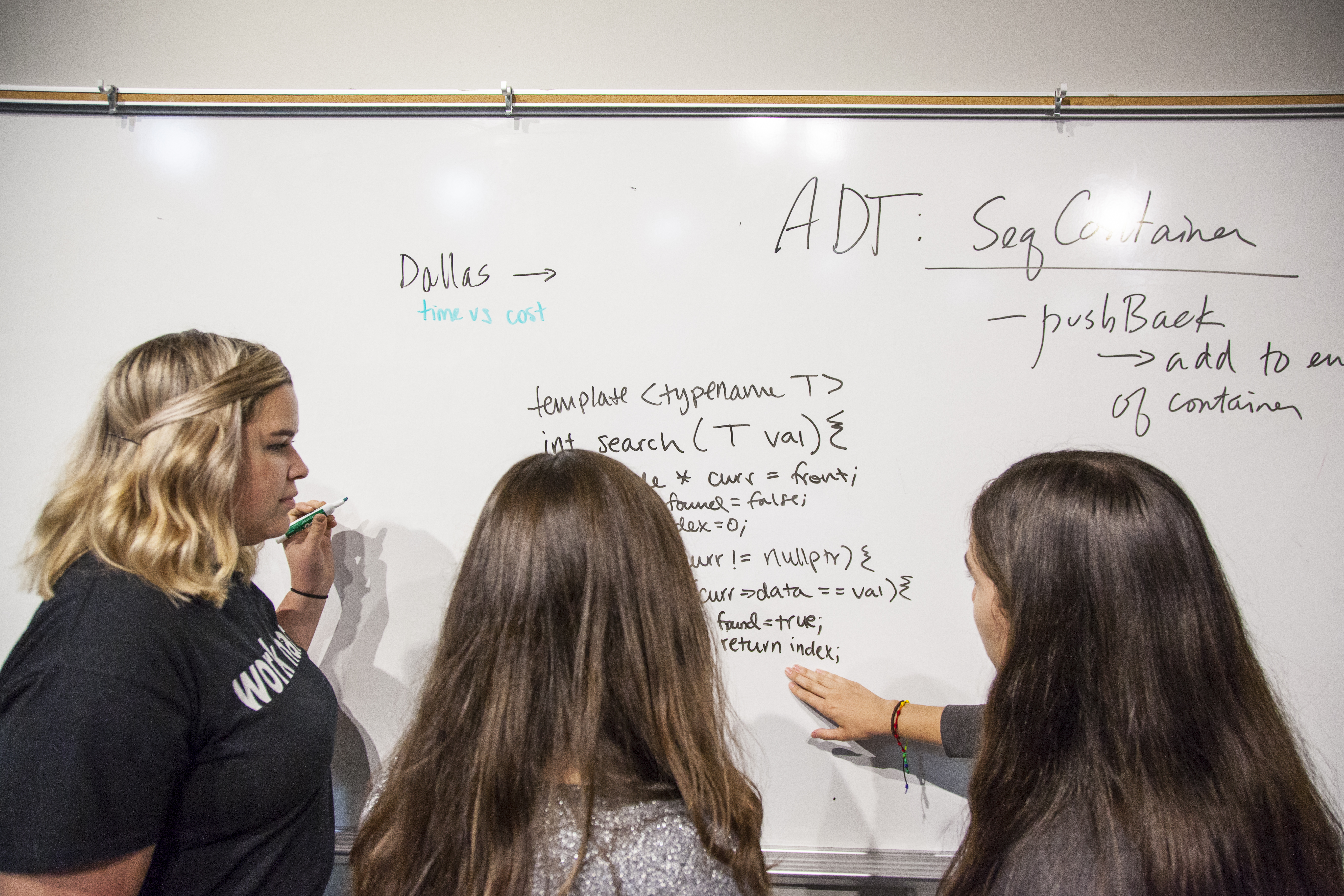 Image of three students working on a project with a dry erase board