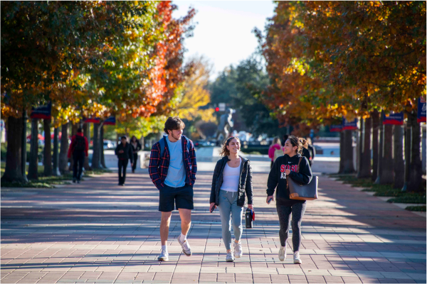 3 students walking across campus together and talking 