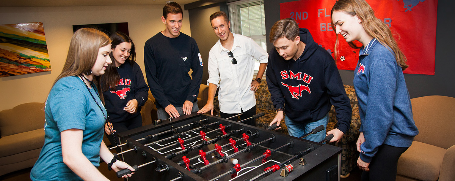 A crowd of people gathered around a foosball table while two players compete against eachother. 