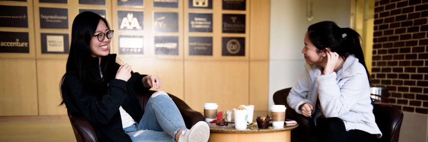 Two students relaxing and talking in lobby with coffee