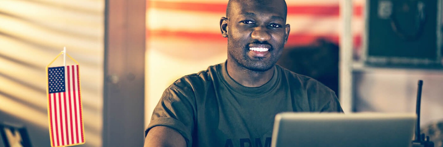 Man sitting in front of a laptop computer smiling and looking at the camera