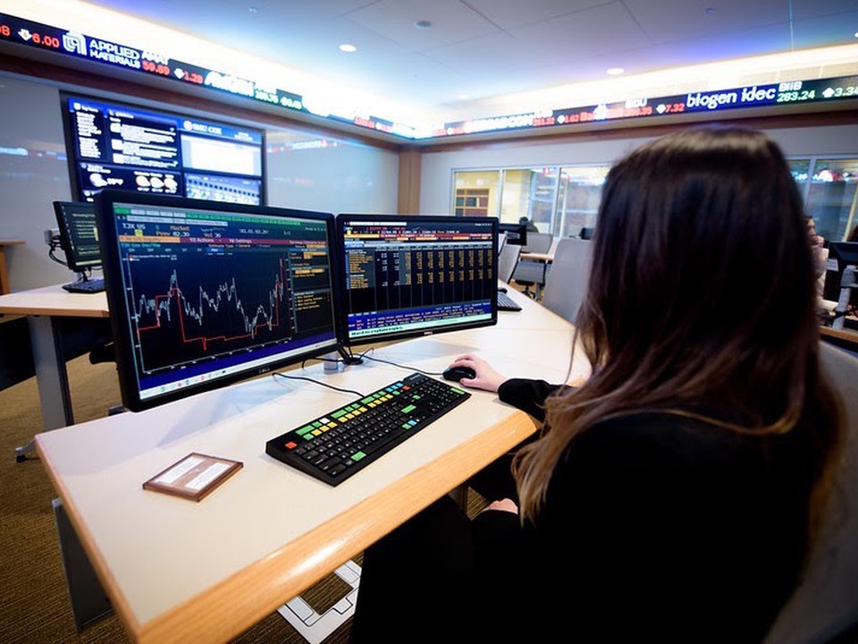 An SMU Cox Online MBA student sits in front of multiple computer screens and analyzing the data and charts on them