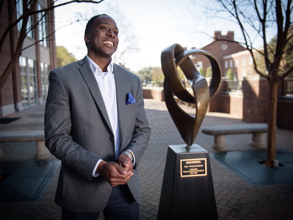 A SMU Cox Online MBA faculty member stands next to a commemorative statue
