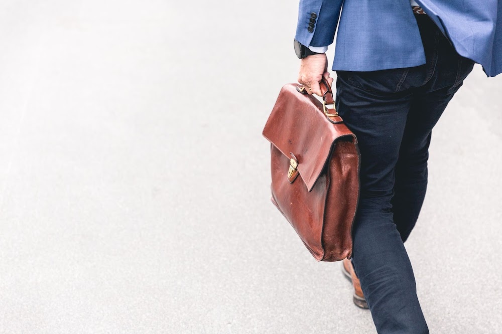 A man walking with a brown leather briefcase.