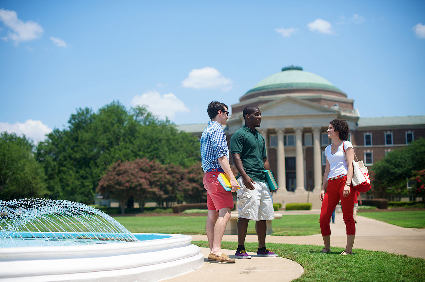 Three students by a fountain, Dallas Hall in the background.