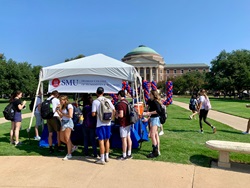 Students stand in line to get Dunkin Donuts under a white tent and Dedman College banner on Dallas Hall Lawn.