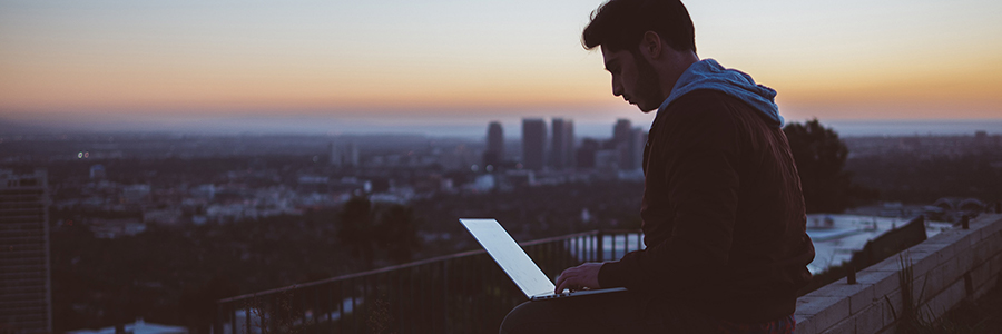 Man sitting on balcony using a laptop.