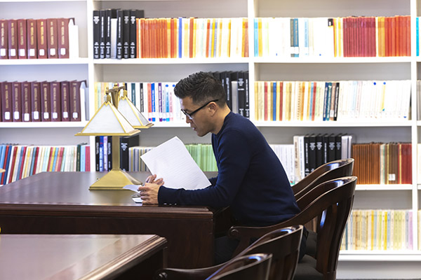 faculty member reading at a table in front of book shelves