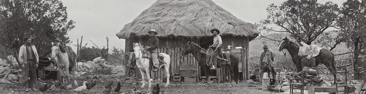owboys in front of small house with thatch roof on ranch, ca. 1900