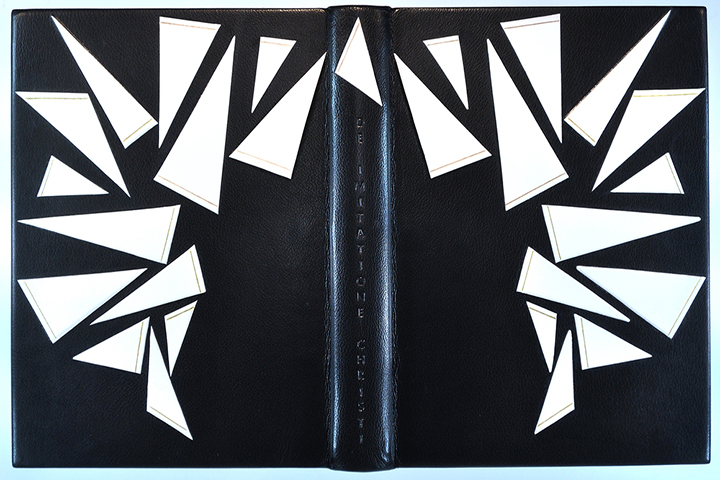 A book bound in black with white triangles in the shape of a crown. "De imitatione Christi" is engraved on the spine.