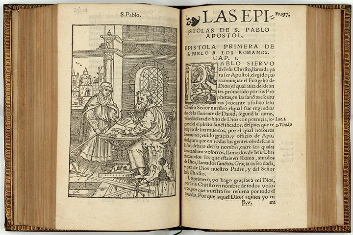 An open Spanish Bible, on the left page is a woodcut of St. Paul at his desk. The right page begins the text from Romans.
