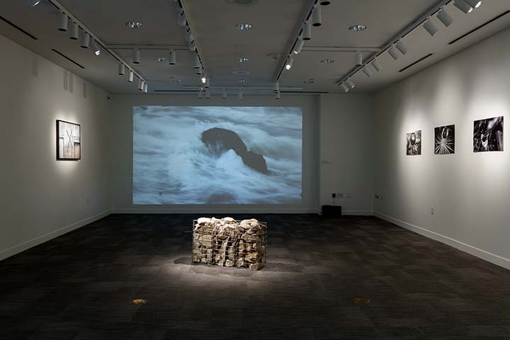 Artwork in the Hawn Gallery including photographs, a sculpture, and an image of water projected on a screen