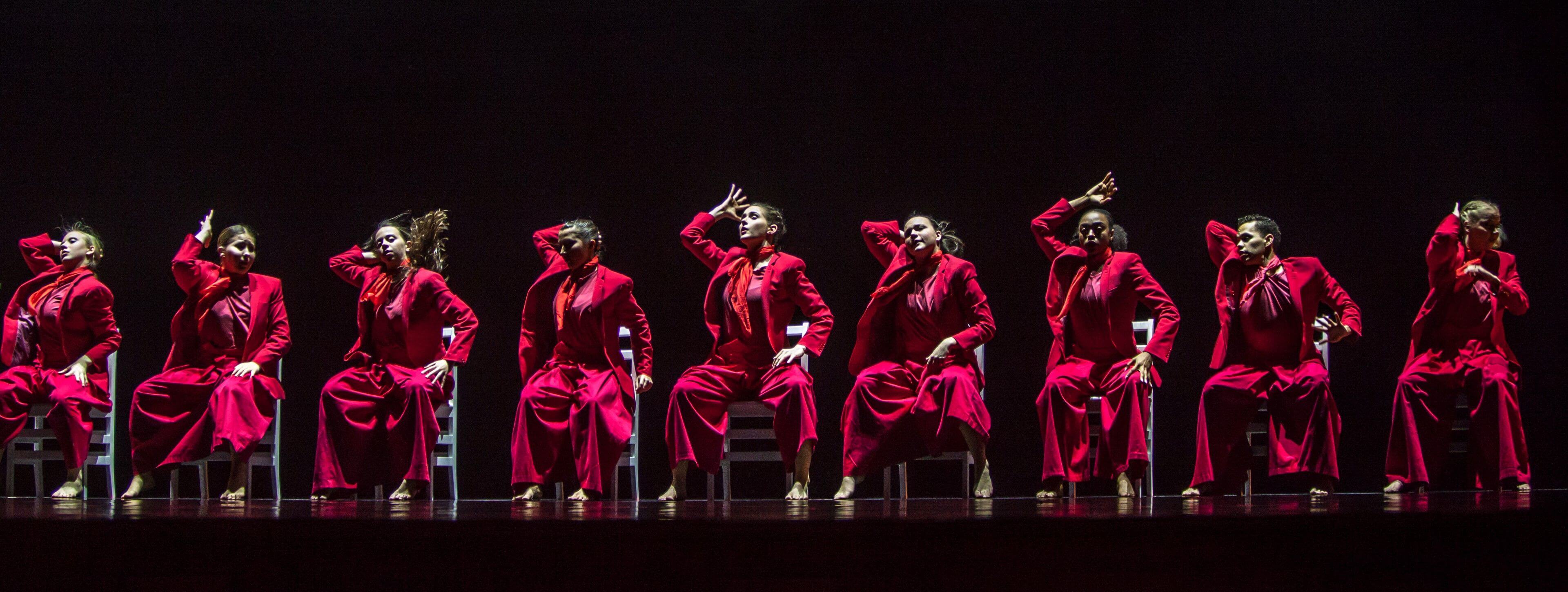 dancers in red sitting on chairs against a black background