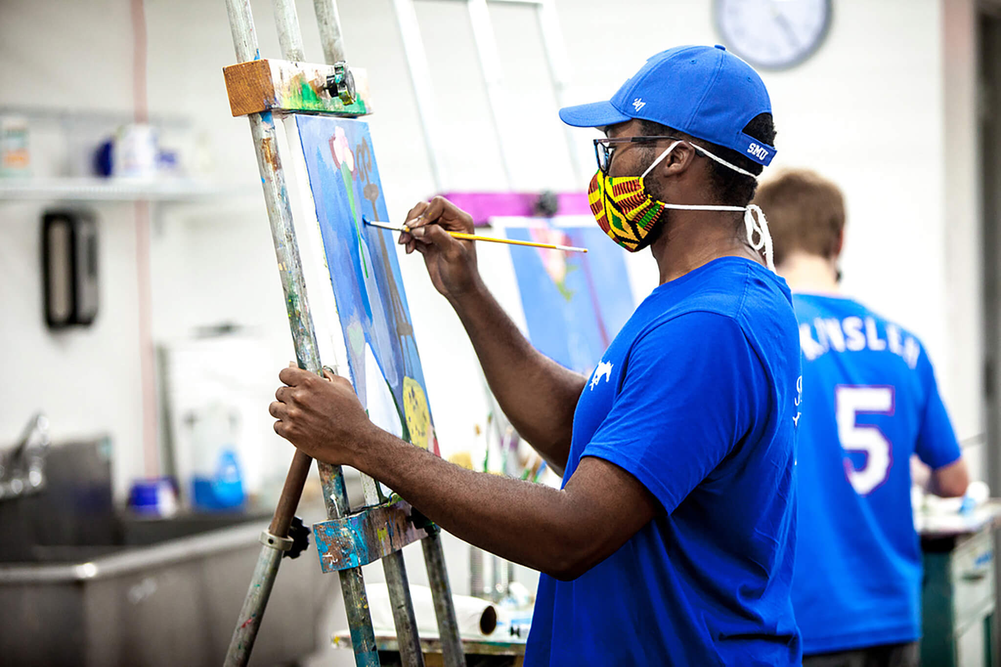 black student in blue shirt painting at a canvas