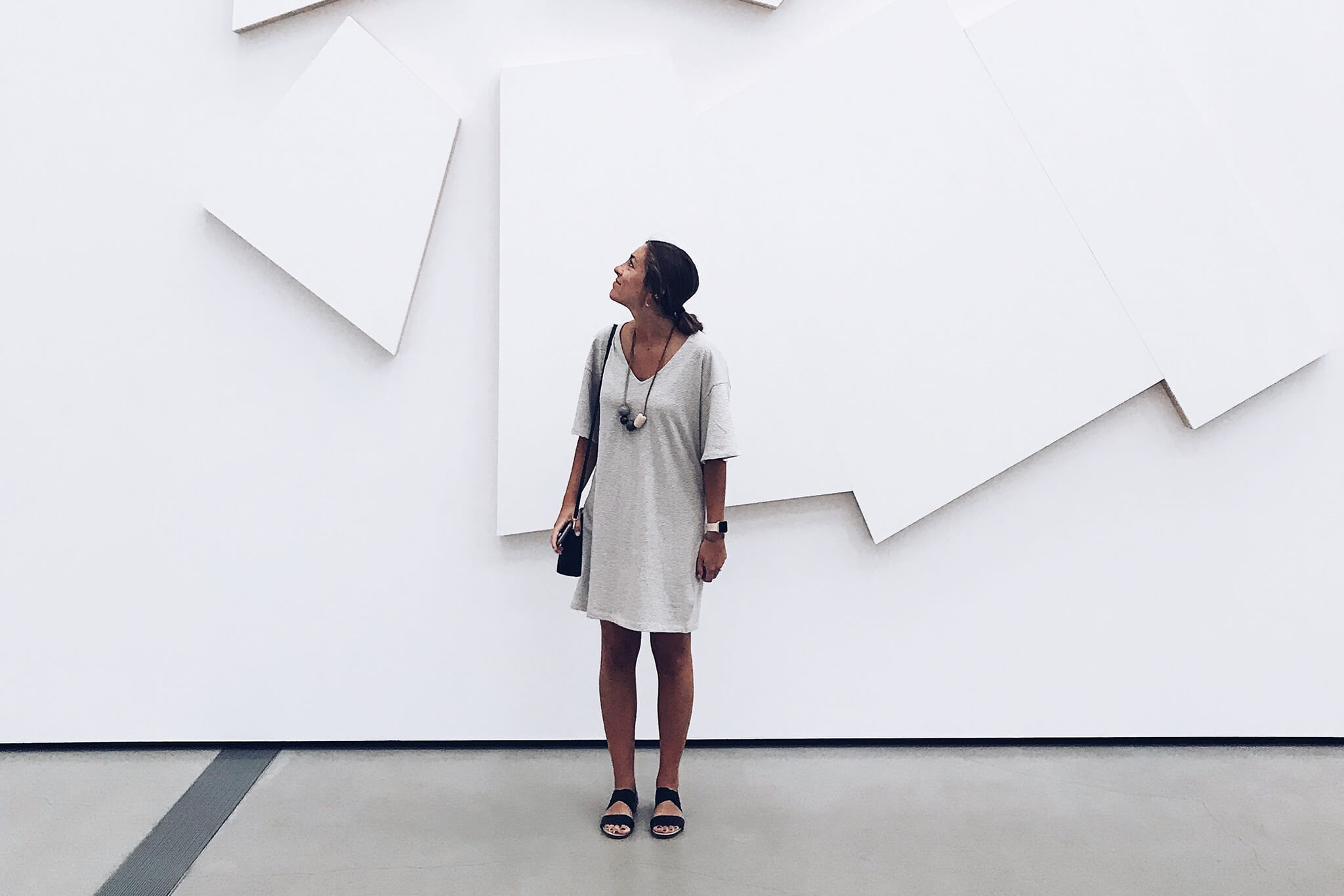 woman in white dress standing in front of a large piece of white art