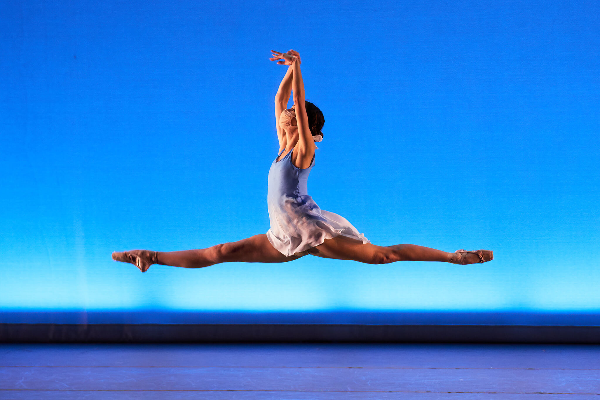Dancer in white costume against a blue background jumping