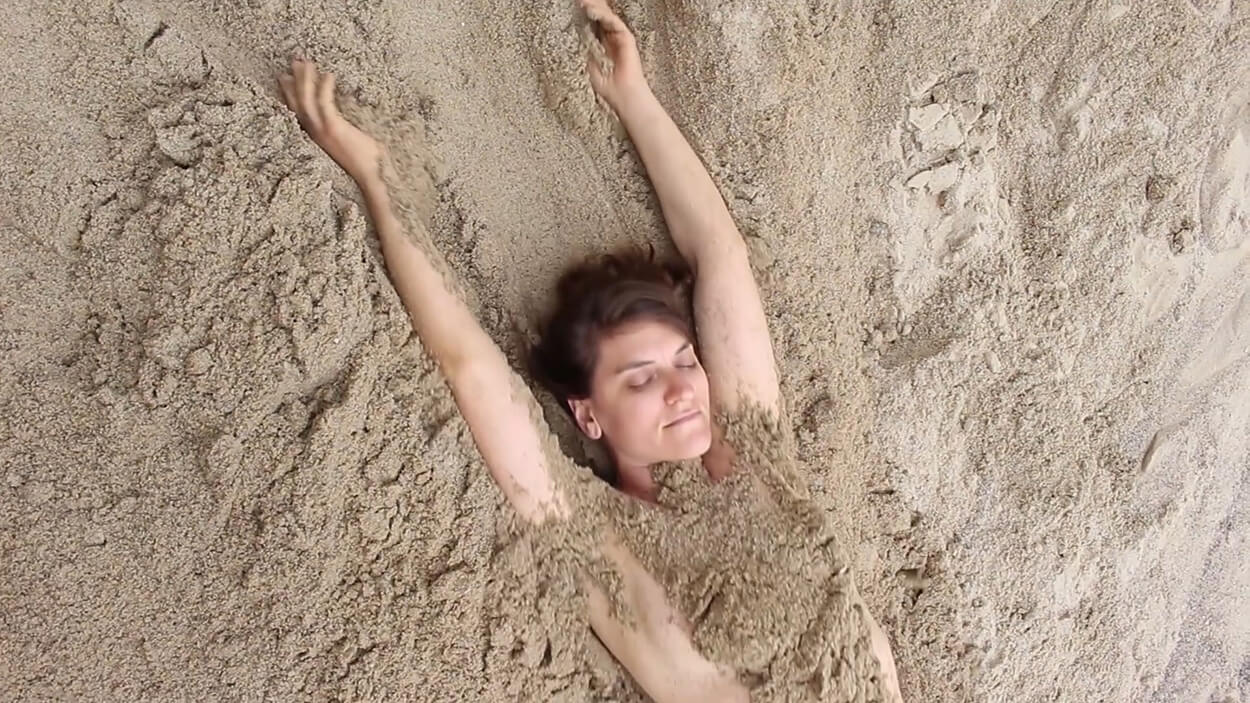 scene from Amber Bemak's experimental short film, "Goodbye Fantasy". Woman on a beach covered in sand