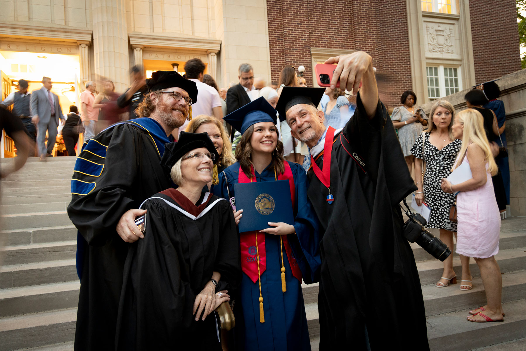 A graduate takes a selfie with a group of their professors following the 2023 Degree Recognition Ceremony.
