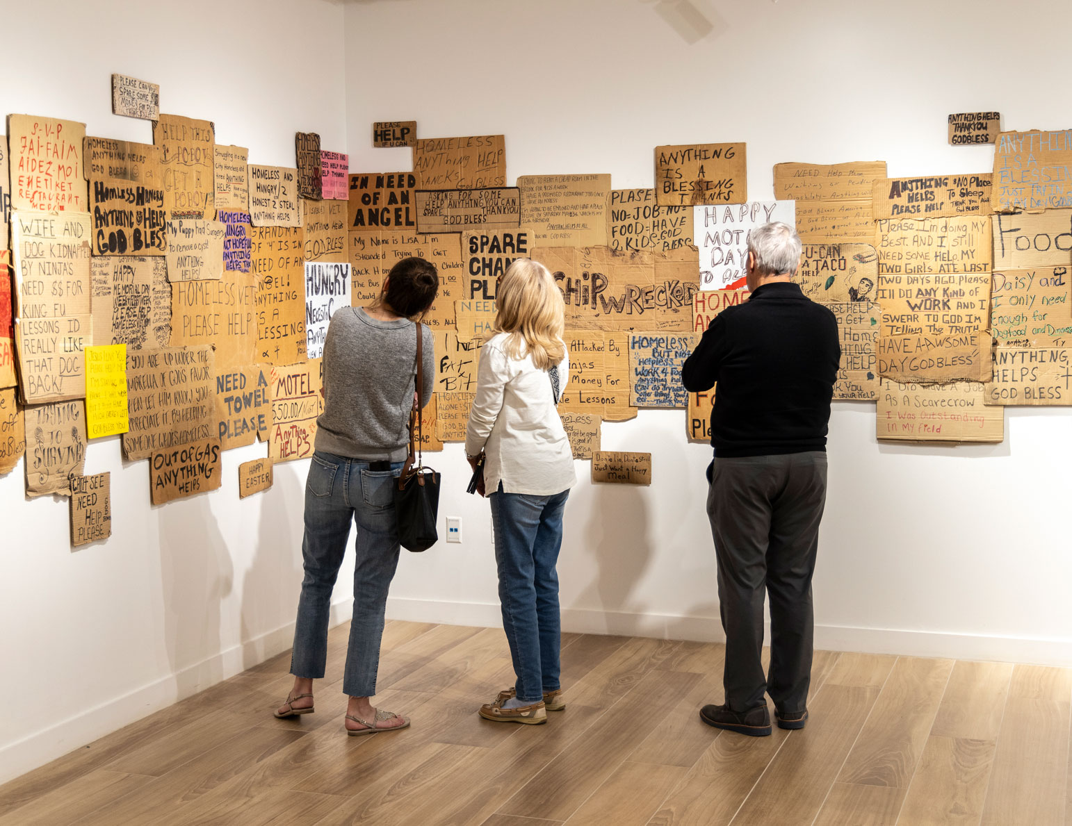 Patrons examine a collection of homeless signs in the "HOME? Humanizing the Homeless: Portraits and Signs" exhibition.