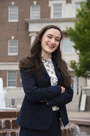 Portrait of SMU junior Gabrielle Gard, pictured in front of SMU building in a blue blazer and white button up with a blue flower pattern