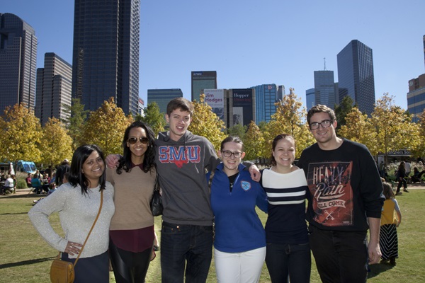 Six students stand in front of iconic Dallas buildings with their arms around each other