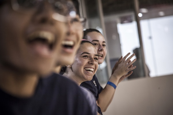 4 students laughing while looking at an object of attention that is out of the camera's view