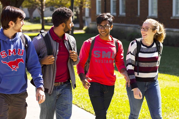 Four students talking to each other while walking along the pathway on Dallas Hall lawn