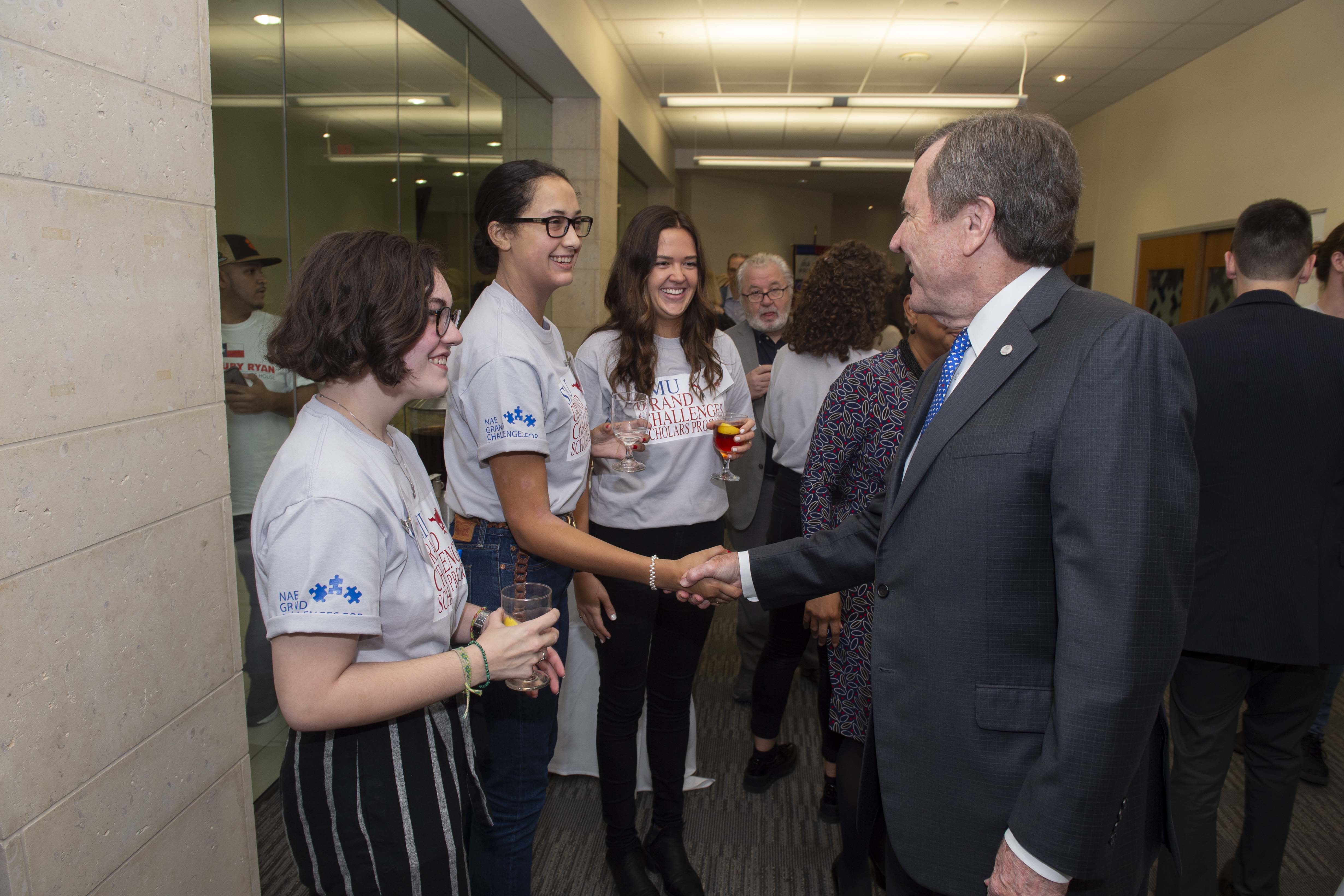 Three female President's Scholars engaged in conversation with University President Robert Gerald Turner. The middle student is shaking his hand.