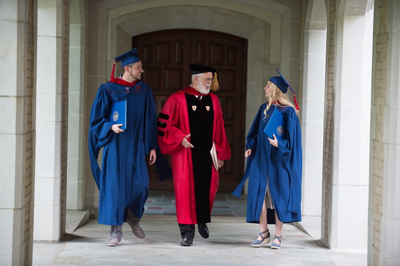 faculty member walking with 2 students at graduation