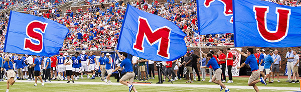 Exciting SMU football game as students enthusiastically run with large SMU flags.