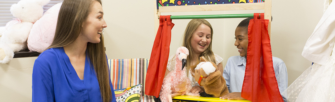 Counselor with two children playing with hand puppets.