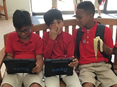 Three boys engrossed in work, using tablets, on a bench in a middle school setting."