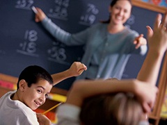 Students raising hands in math class with teacher looking on