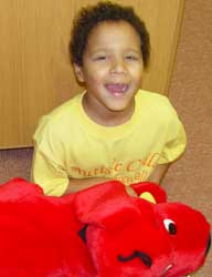 A young boy sits on the floor, holding a red stuffed animal close to his chest.