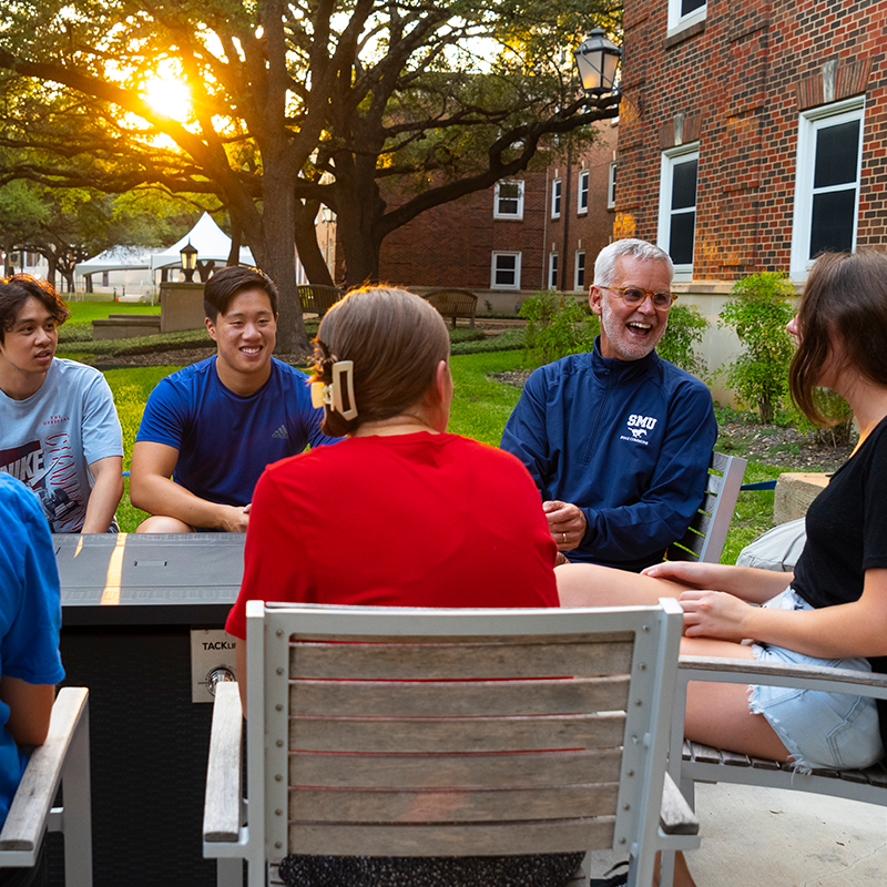 Students and a professor chatting outdoors at a table at the residential commons
