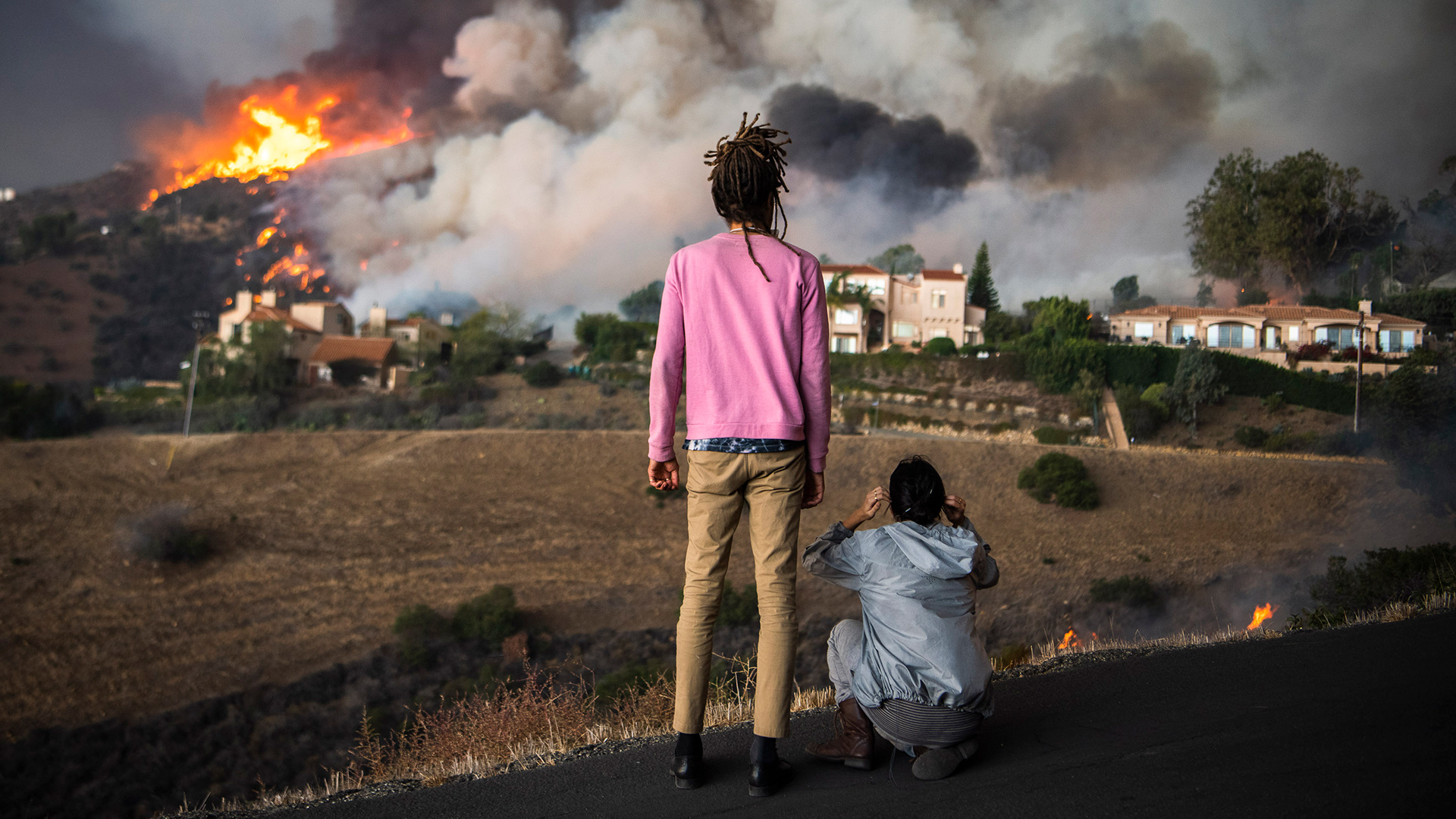 A photo of two people watching a home go up in flames.