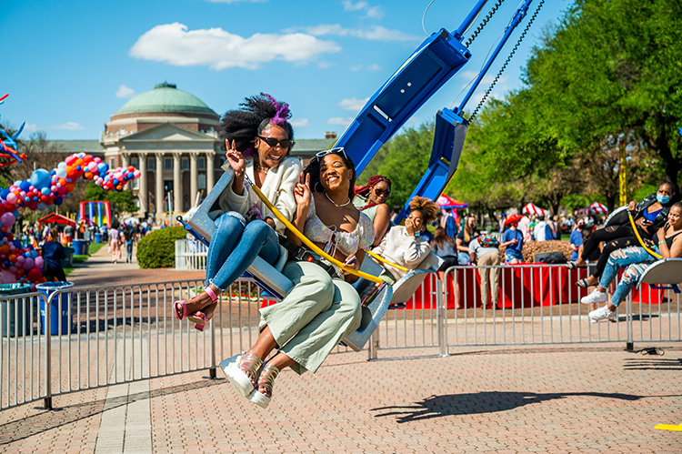 People on a carnival ride in front of Dallas Hall