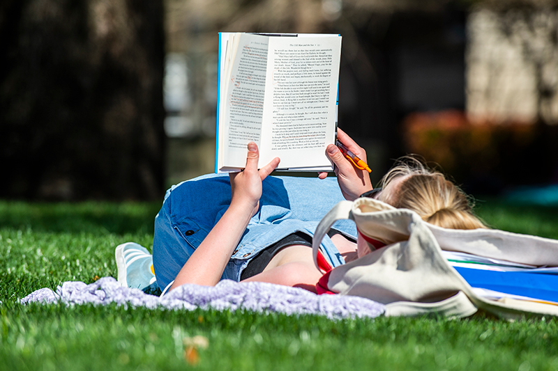 Person reading book on the lawn of Dallas Hall