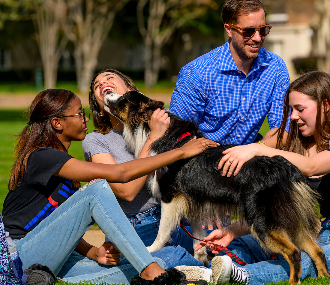 People gathered around a dog on the front lawn of Dallas Hall