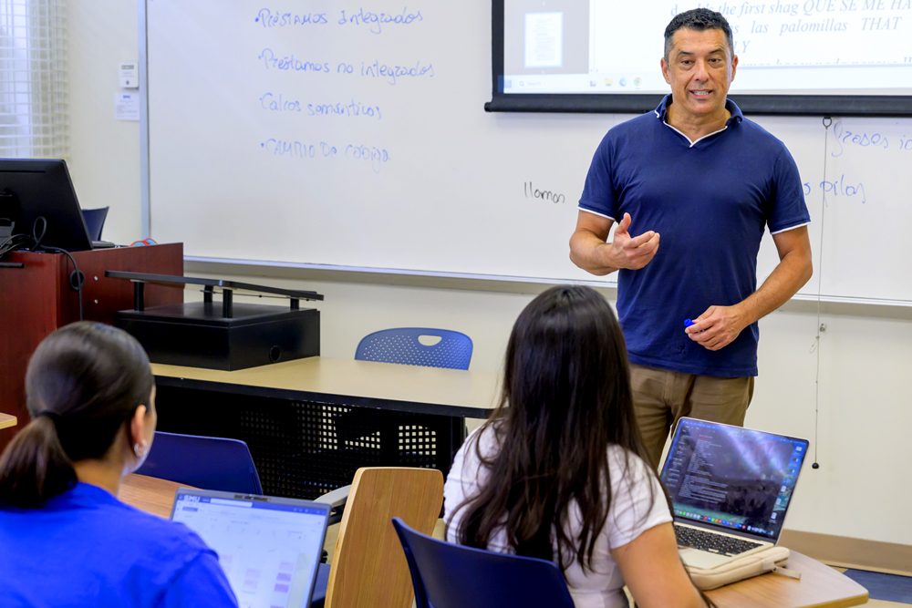 An instructor leads a classroom discussion with students using laptops.