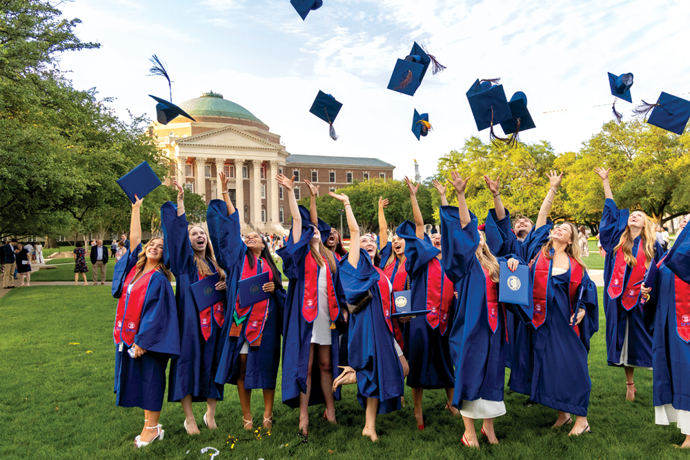 SMU graduates in blue gowns toss their caps into the air on campus.