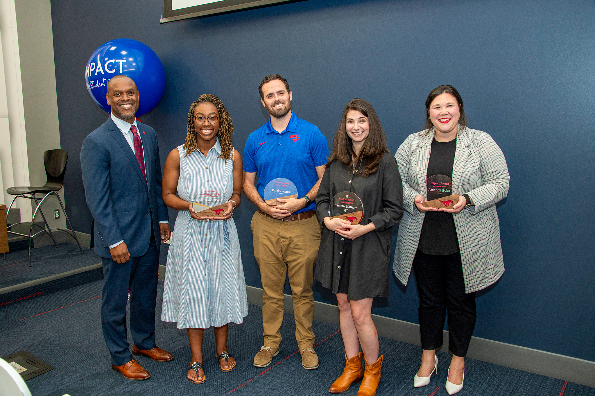five people standing in front of blue wall holding award plaques