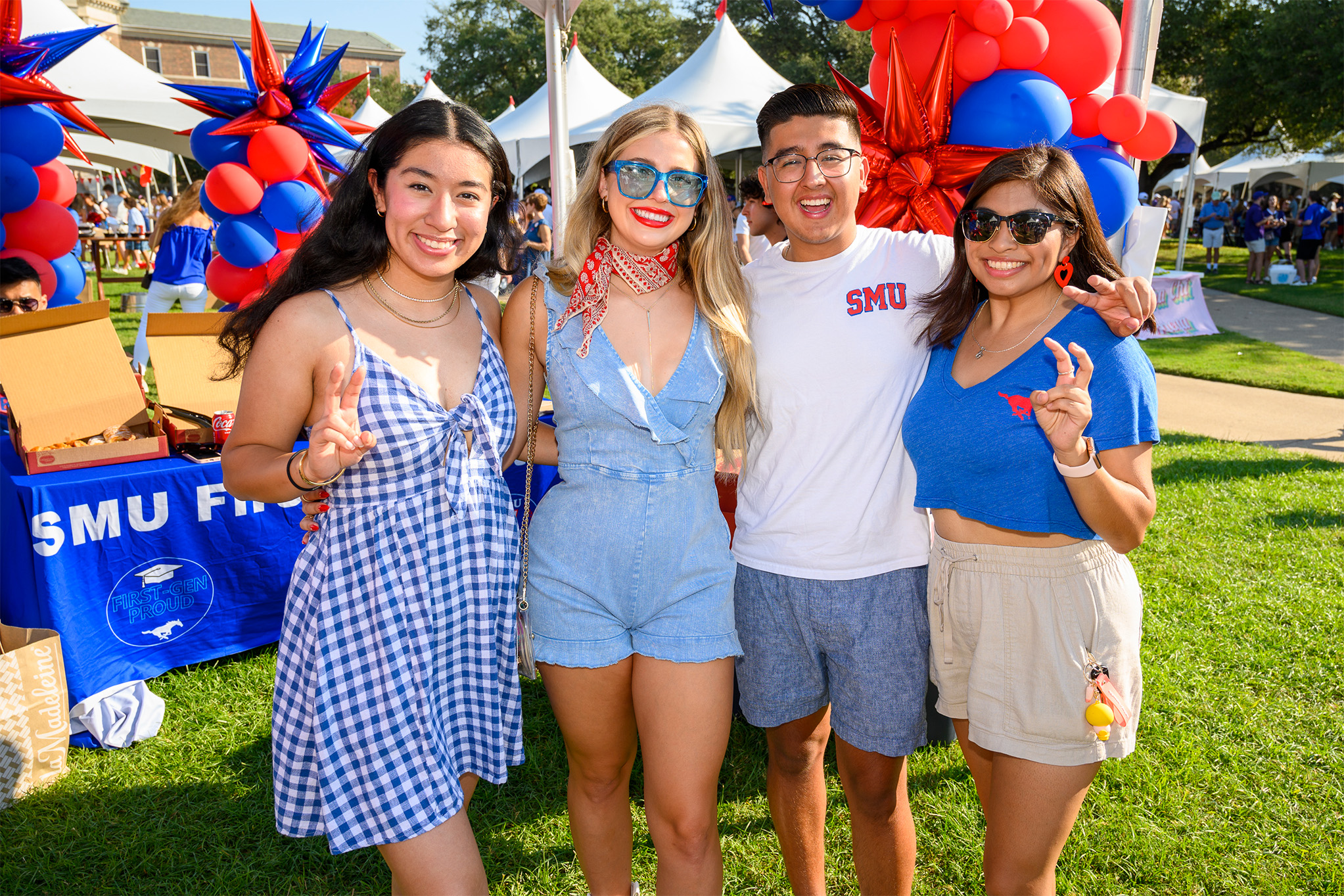 four students outside standing in front of a table and balloons at an outdoor event