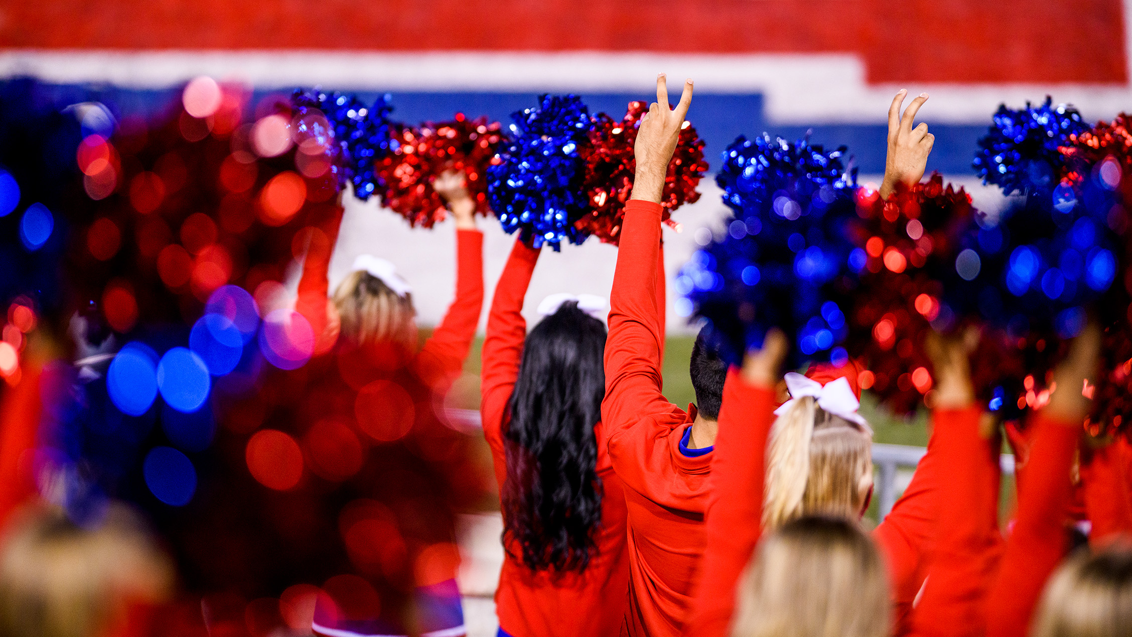 cheerleaders with red and blue poms and holding up pony ears hand sign