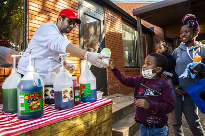An SMU student serves a child a snow cone at an Engage Dallas event.