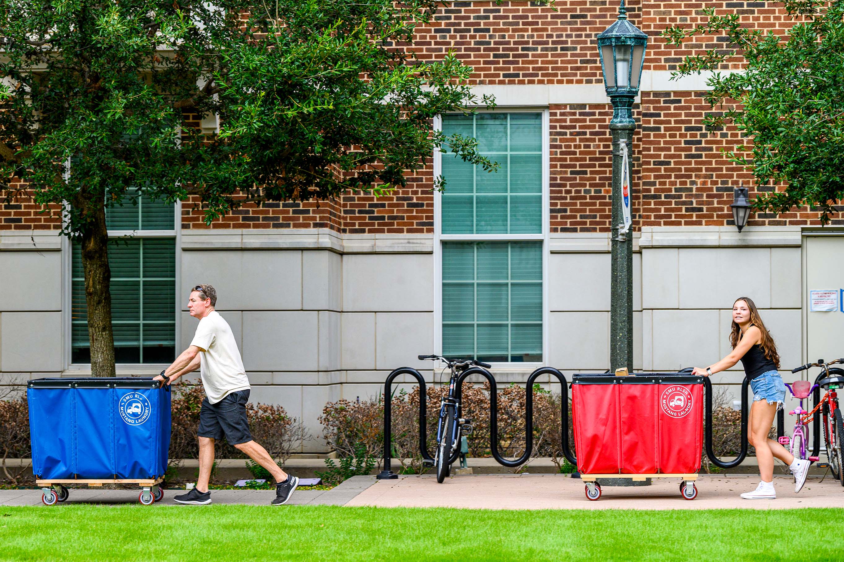 a parent and a student pushing a blue moving bin and a red moving bin outside
