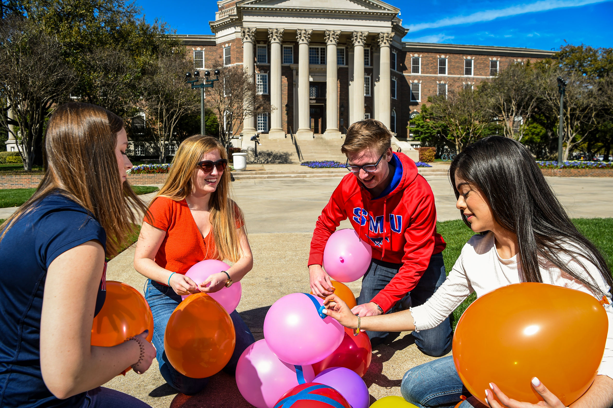 Four students working together to build a tower of balloons on Dallas Hall lawn. 