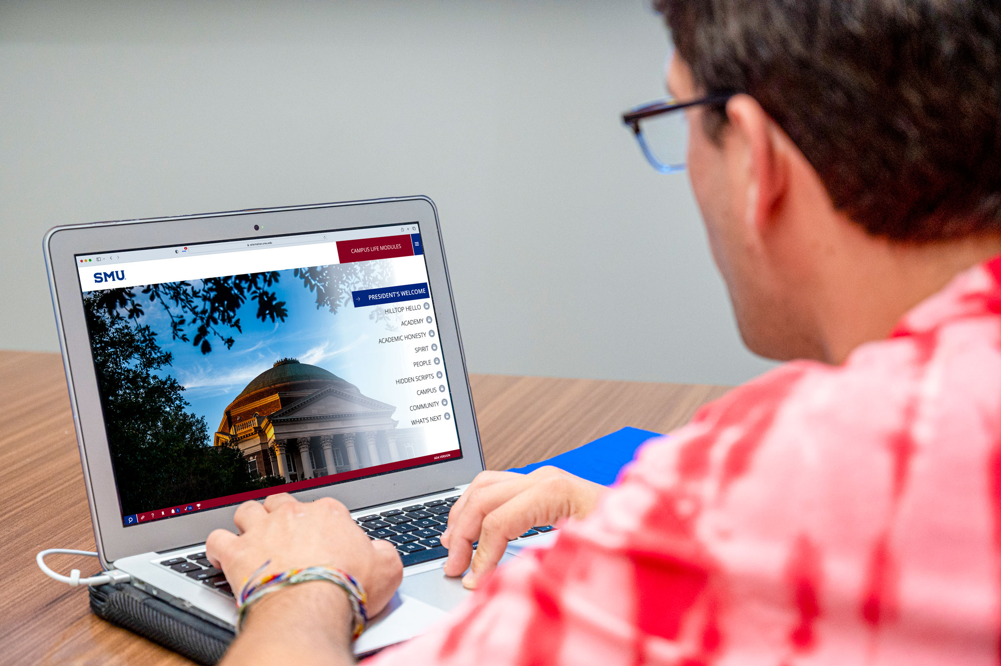 student in red shirt with glasses looking at orientation website on laptop